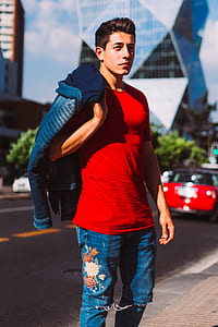 man holding jacket standing wearing red shirt and blue jeans near road thumbnail