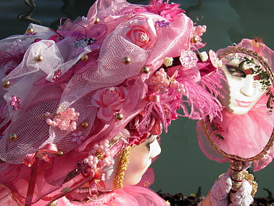 person holding hand mirror wearing white and pink floral accent mask and fascinator thumbnail