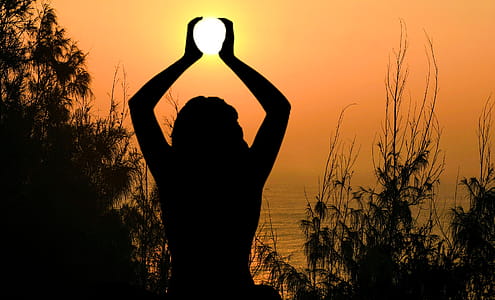 Silhouette of woman doing yoga, cradling the sun in her hands. thumbnail