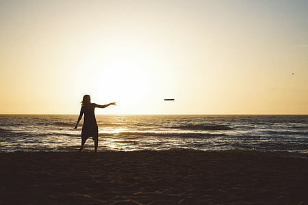 silhouette of woman throwing frisbee disc on beach thumbnail