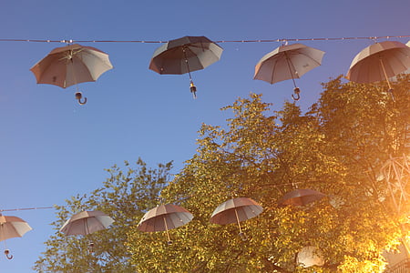 low angle photography of two lines grey umbrellas hanging on black wire beside green leaf trees under blue sky at daytime thumbnail