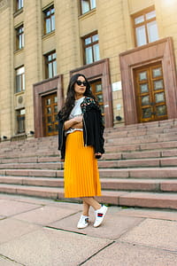 Women Wearing Black Jacket and Pleated Yellow Skirt Standing on Brown Floor thumbnail