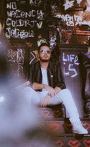 man wearing black and white striped jacket sitting on black stair thumbnail