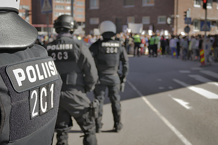 three police in front of crowd in the middle of street at daytime thumbnail