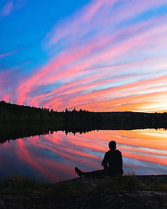 silhouette of person sitting in front of lake during daytime thumbnail