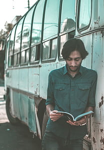 man reading book while leaning on buss thumbnail