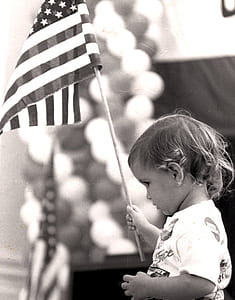 grayscale photo of toddler holding U.S.A. flag thumbnail