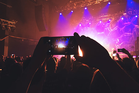 A person photographer in the crowd taking a photo with their mobile phone at a music concert festival thumbnail