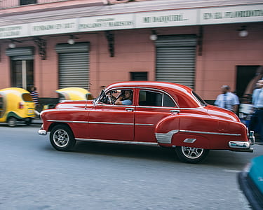 classic red sedan passing people and autorickshaws during daytime thumbnail