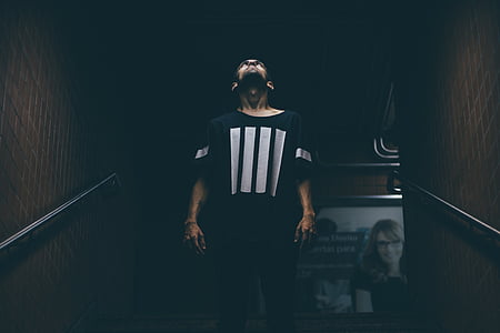 man wearing white and black scoop-neck t-shirt standing on stairs thumbnail