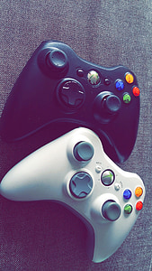 two black and white Xbox 360 controllers on gray textile thumbnail