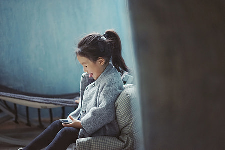 girl wearing gray coat sitting on sofa using mobile phone thumbnail