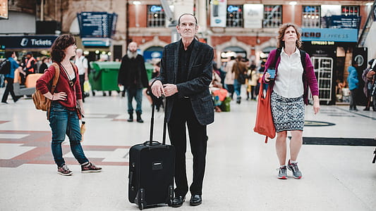man wearing black suit jacket standing while holding luggage bag thumbnail