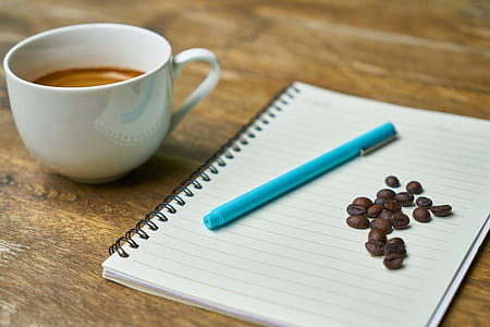 teal ball-point pen on white notebook beside coffee bean thumbnail