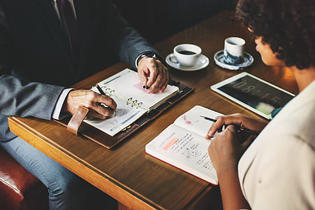 two people sitting next to table writing on notebooks thumbnail