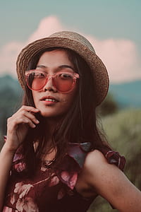 woman wearing gray sun hat, pink sunglasses, and red floral sleeveless top thumbnail