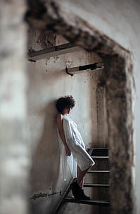 woman in white dress leaning on wall near stairs thumbnail