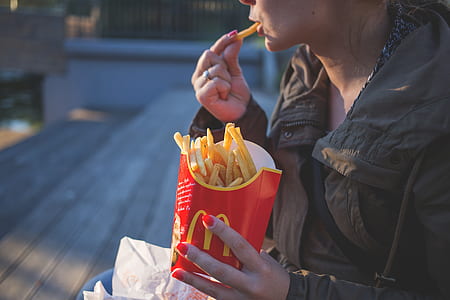 tilt-shift lens photo of woman sitting on a bench eating McDonald's fries thumbnail