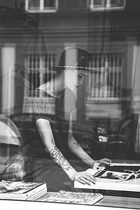 grayscale photo of woman wearing black short-sleeved dress and black hat reading magazine thumbnail