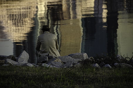 man sitting on grass facing body of water thumbnail