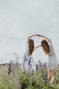 two women holding hands surrounded by purple petaled flowers thumbnail