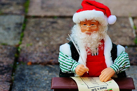 Santa Claus doll holding feather pen sitting in front of brown desk thumbnail