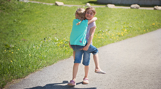 girl carrying girl walking concrete road near grass field thumbnail