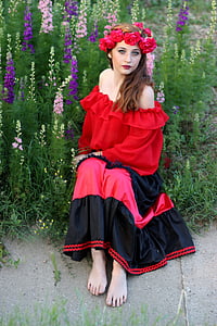 woman in red and black dress sitting beside purple and pink flowers thumbnail