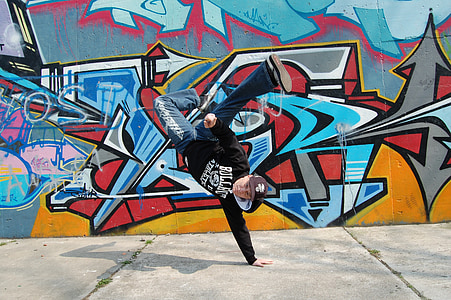 man wears black hoodie doing one hand stand near multicolored wall graffiti during daytime thumbnail