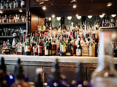 stack of assorted liquor bottles on white table and black shelf thumbnail
