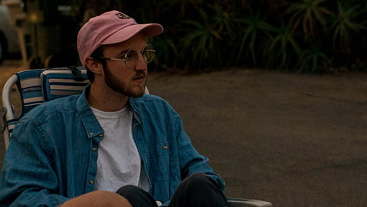 man sitting on lounger chair wearing blue jacket and pink cap outdoor thumbnail