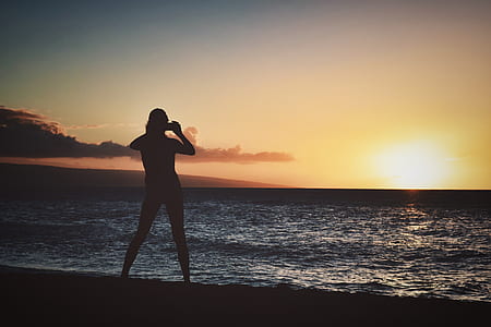 Silhouette of Woman Holding Camera Near Seashore during Golden Hour thumbnail