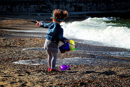 toddler in jacket holding bucket standing on seashore thumbnail