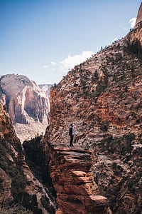photo of man sanding on cliff facing mountain thumbnail