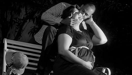 grayscale photo of man kissing woman while sitting on bench thumbnail