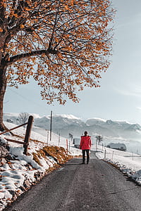 woman wearing red jacket standing in the middle of road between snowy field thumbnail