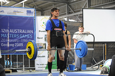 man in black top carrying yellow and blue barbells thumbnail