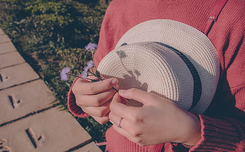 Person Wearing Sweater Holding Flower and Hat thumbnail