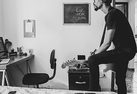 grayscale photography of man playing guitar in room thumbnail