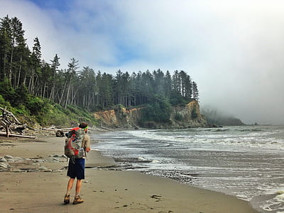 man with backpack walking near body of water during daytime thumbnail