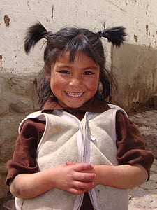 smiling girl wearing beige knit zip-up vest and brown collared shirt near gray concrete wall thumbnail