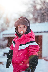 Toddler Boy Wearing Red and Black Winter Jacket and Gray Ushanka Hat Standing on Snow Covered Field thumbnail
