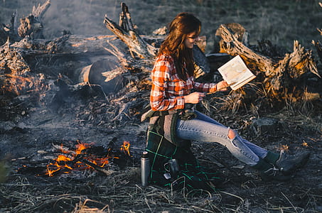 shallow focus photography of woman near bonfire reading book thumbnail