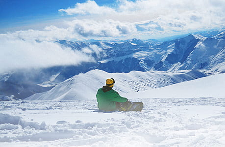 man in green jacket sitting on snowy land thumbnail