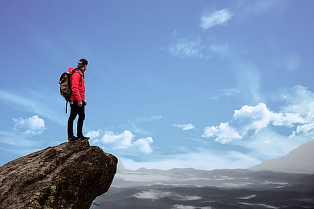 man wears red jacket standing on rock formation at daytime thumbnail