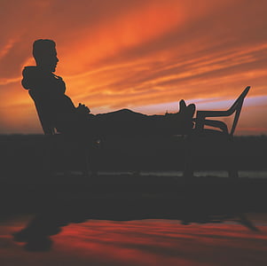 silhouette of man leaning on backrest with feet on other chair during daytime thumbnail