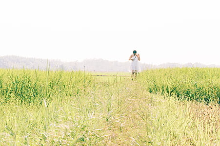 Woman Wearing White Sleeveless Dress Walking on Green Grass Field Under White Sky thumbnail