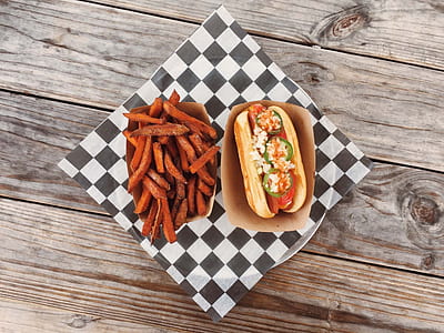 hot dog sandwich and sweet potato fries on plate over wooden surface thumbnail