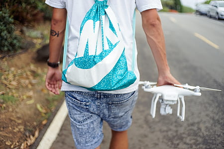 person carrying white quadcopter drone while walking on street during daytime thumbnail
