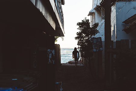 woman walking in between houses near sea shore thumbnail